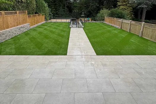 Wide garden view with Grey York Porcelain Paving creating a central path and patio alongside neatly mown artificial lawn.