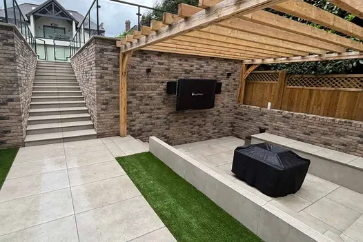 Outdoor entertainment space beneath a timber pergola, finished with Grey York Porcelain Paving and built-in seating.
