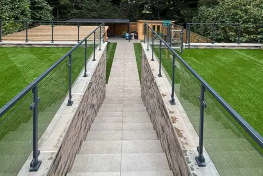 Long descending staircase clad in Grey York Porcelain Paving with glass balustrades and raised lawn terraces.