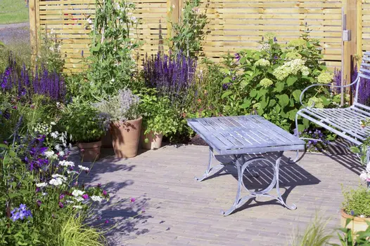 Gromo Antica Clay Pavers with metal garden furniture, encircled by vibrant green and purple plants.