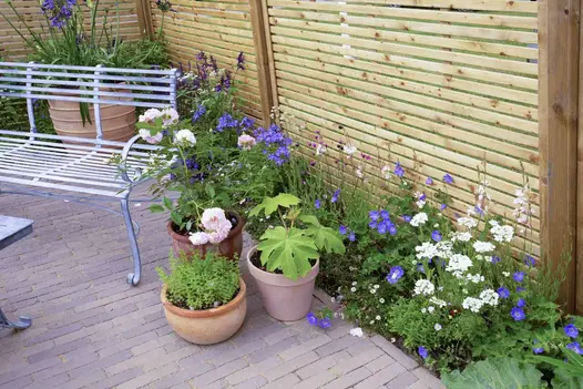 Metal garden furniture on Gromo Antica brick paving, with potted plants and abundant green and purple foliage around.