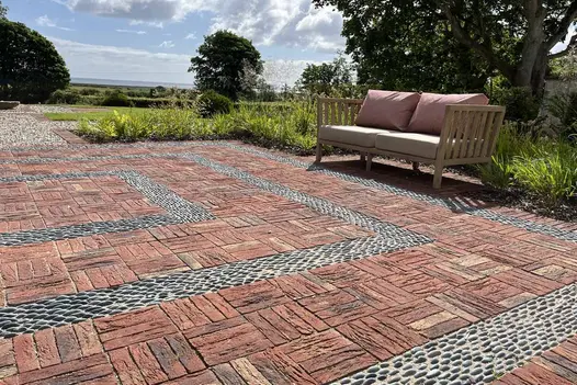 2-seater outdoor sofa at edge of rectilinear area paved with Old English Belgian bricks laid basketweave with pebble detailing.