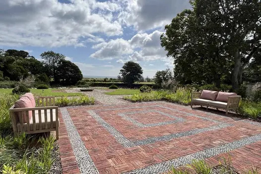 Old English Belgian bricks laid basketweave with pebble detailing in square with 2 2-seater outdoor sofas facing each other.