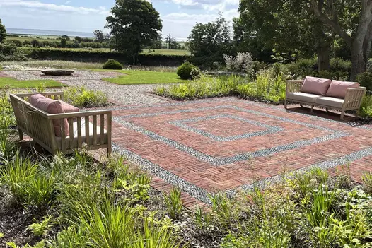 2 2-seater outdoor sofas face each other across square paved with Old English Belgian bricks laid basketweave with pebble detailing.