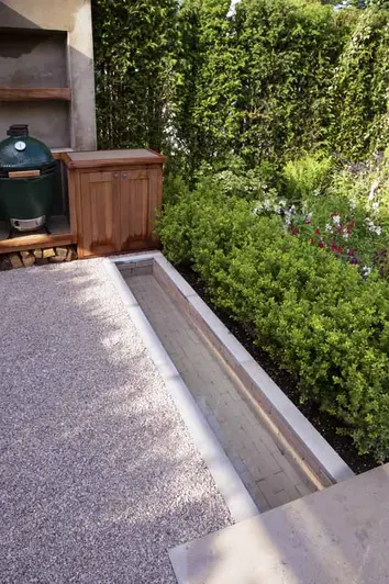 Gromo Antica clay pavers create underwater path leading to the BBQ area, serving as a water feature next light-coloured pebbles.