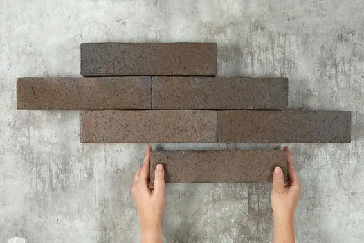 Hand places 6th brick at bottom of formation of 5 Chelsea clay pavers arranged in 3 rows of 1 or 2 bricks each.