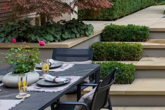 Dining table sits at the bottom of 3 britannia buff yorkstone steps, with pencil round coping stones topping the raised flowerbeds.