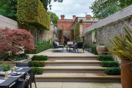 Britannia Buff Yorkstone bullnose steps rise to narrow, paved walled garden with tall metal gates at end and beds down each side.