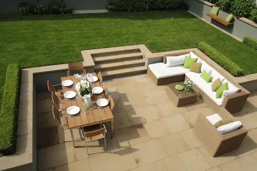 Birds eye view of sunken patio with dining table and lounge area. Britannia buff yorkstone used as paving, steps and pencil round coping stones.