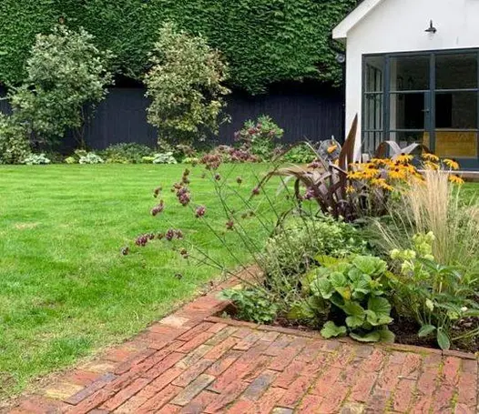 Fenced garden with large lawn and garden room on 2 sides of area paved with Old English Belgian bricks. 