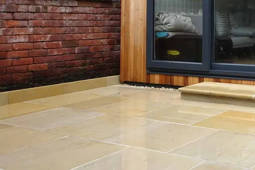 Close up of harvest sawn sandstone paving in wet conditions also shows one bullnose step leading to garden building.