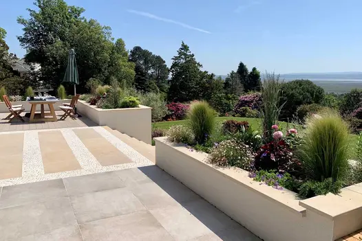 Countryside views seen from multi level garden with deck and patio, steps lead down to lawn with raised flowerbeds using harvest coping stones.
