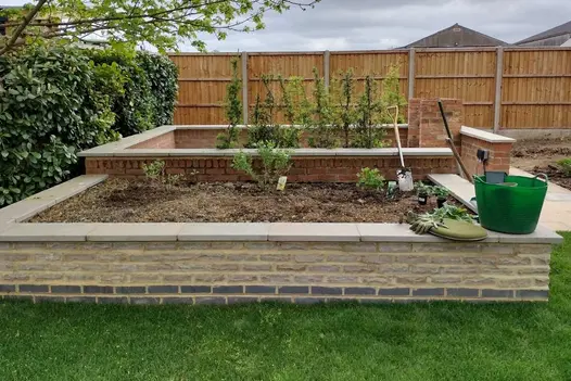 Trug and kneeler on wide Heath smooth sandstone pencil round coping stones of raised brick-built bed. Design by Judi Samuels.