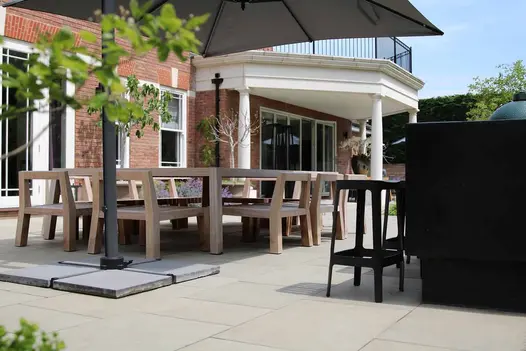 Heath smooth sandstone patio paving at rear of brick house with 5 sided balcony. Cantilevered parasol shelters dining set.