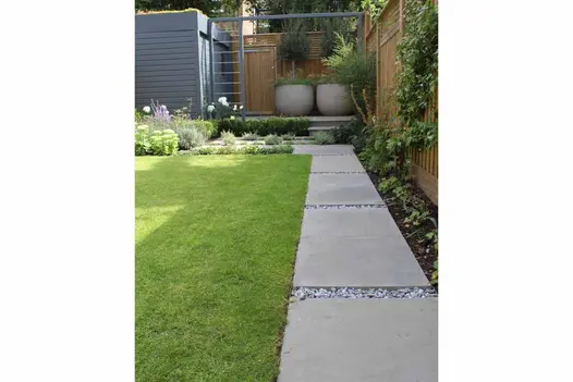 Narrow path of Heath sawn sandstone slabs with wide gravel joints runs between lawn and very narrow border towards end of garden.