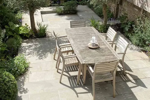 View down onto narrow town garden paved on different levels with Heath smooth sandstone paving. Wooden dining set in foreground. 