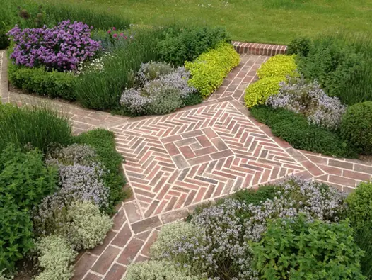 Unique X-shaped path sees dorset antique clay pavers lead to square pattern using herringbone style, flowerbeds surround.