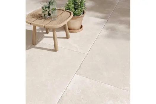 Light-toned Heritage Chalk Premium Italian Porcelain Paving with soft stone texture, shown with a wooden table and potted plant.