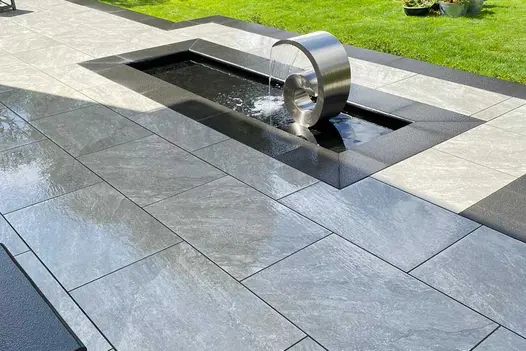 Close up view showing wet Kandla Grey Porcelain Pavings unique texture, darker porcelain surrounds water feature.