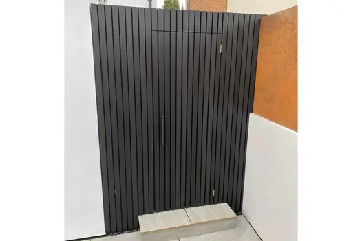 Close-slatted fence of Dark Ash composite battens, incorporating almost invisible matching door in open-air corner between 2 walls.