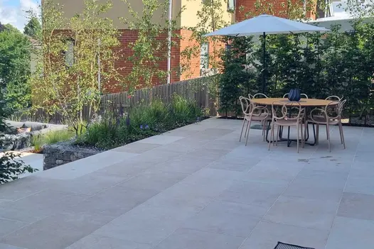 Round table and chairs with separate parasol on white terrace paved with Egyptian beige smooth limestone, overlooking garden below.