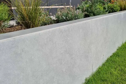 Retaining bed filled with low shrubs and grasses and faced with Hydra Plomo light grey porcelain external cladding. 