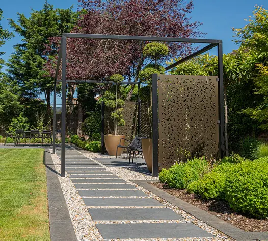Down side of garden, straight path of Black Granite plank paving and buff gravel runs past seating area with pierced metal screens.