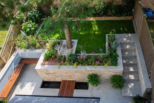 Overhead view of deeply terraced garden with lower area paved with Faro porcelain slabs rising via 7 narrow steps to lawn and beds.