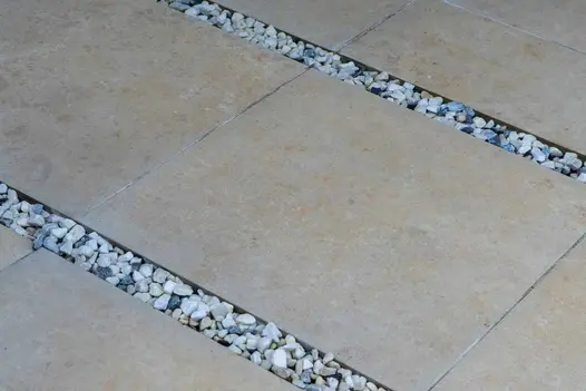 3 strips of Jura Beige porcelain paving separated by wide joints of small blue and white pebbles. Design by Imago Gardens.