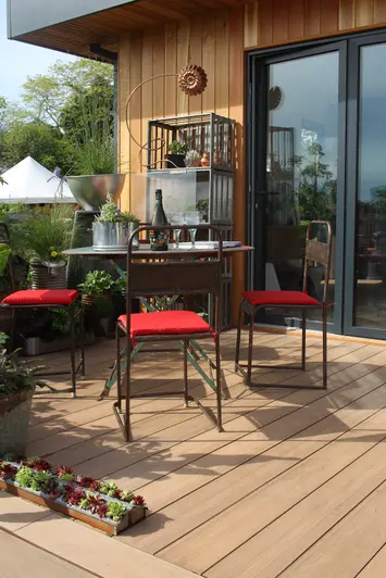chairs with red cushions sit around table with wine and glasses prepped, mocha designboard decking runs underneath.