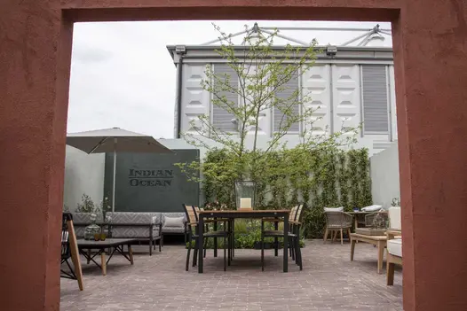 Indian Ocean trade stand seen through rectangular entrance, with Verona clay paving, furniture sets and white walls with planting.