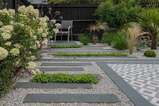Staggered Charcoal Porcelain Planks used as stepping stone patio tiles leading up to seating area with pebbles inbetween.