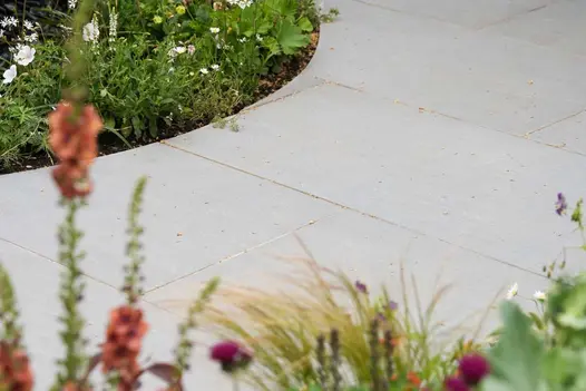 Curved path paved in Trendy Black Porcelain with bordered green plants visible in the background with out of focus colourful plants.