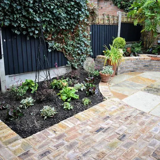 Patio of london mixture clay paver bricks flanked by flowerbed, leads to sandstone circle encased by the belgian bricks.