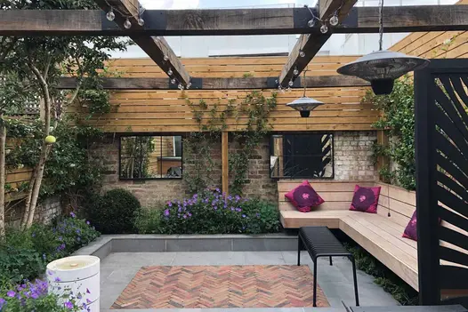 Seville Clay Pavers and Porcelain Paving in a garden with mirrors on the brick walls, a wooden pergola, and lush planting.