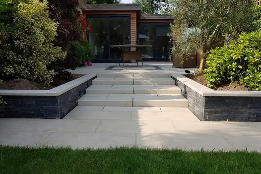 Looking down a garden towards a cedar clad glass fronted garden building sat in top of a Slab Khaki porcelain patio.