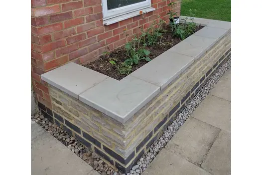 Grey brick raised bed attached to house wall, with Heath smooth sandstone pencil round coping. Design by Judi Samuels.