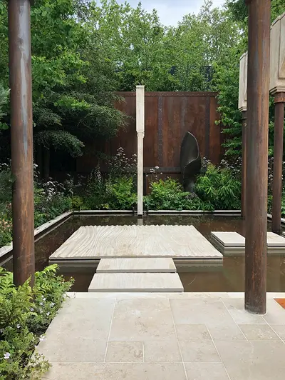 Large textured bespoke slab of Jura Beige limestone in middle of square pond, with matching stepping stones on 2 sides.
