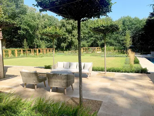 Large garden edged with mature trees, with Jura Beige limestone patio and steps next to house, up to rectangular lawn.