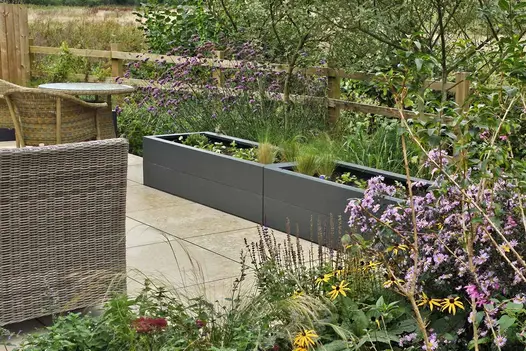 2 grey trough planters on Jura Beige smooth limestone paving laid stack bond in patio next to post-and-rails fence.