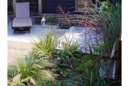 Recliner on Jura Grey smooth limestone paving next to lantern and wooden planting box. Planted bed in foreground.