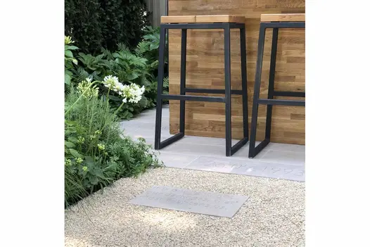 2 metal stools at counter faced with wood sit on Jura Grey smooth limestone paving slabs next to lushly planted beds.