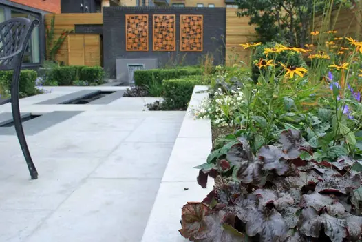 View along coping of raised bed in garden paved with Jura Grey sawn limestone slabs with rill fed by water feature. 