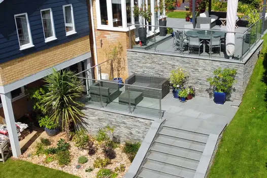 Aerial view of seating areas on 2 terraces with Kandla Grey stone clad retaining walls in steeply sloping garden.