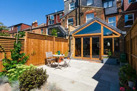 Back of urban terrace house with wood and glass extension and Kandla Grey Indian sandstone patio with bistro set. 