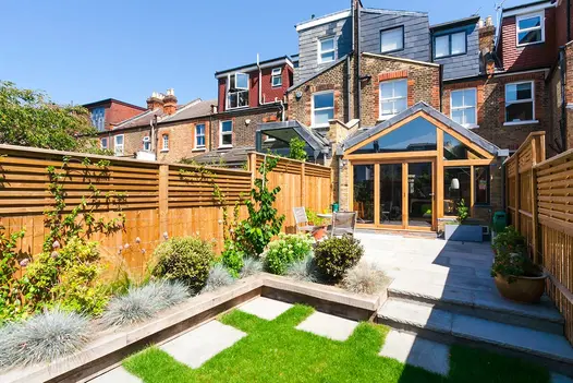 Urban back garden, half lawn, half Kandla Grey sandstone paving, with edge of raised bed as long bench seat.