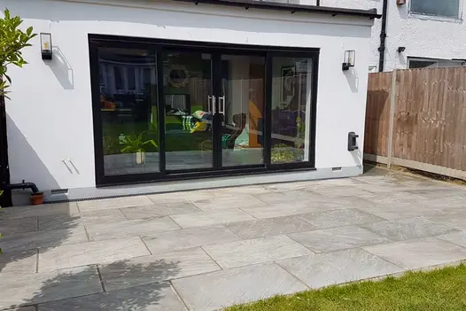 Rectangular patio of Kandla Grey Indian sandstone separates White house with bifold doors from lawn. Design by Silva Tree.