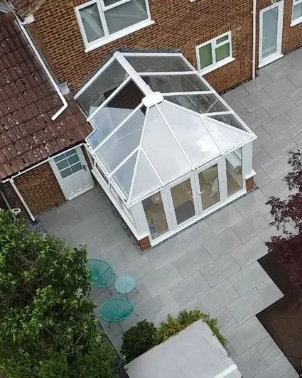 Aerial view of conservatory attached to house surrounded by Kandla Grey outdoor porcelain tile patio, edged with trees and shrubs.