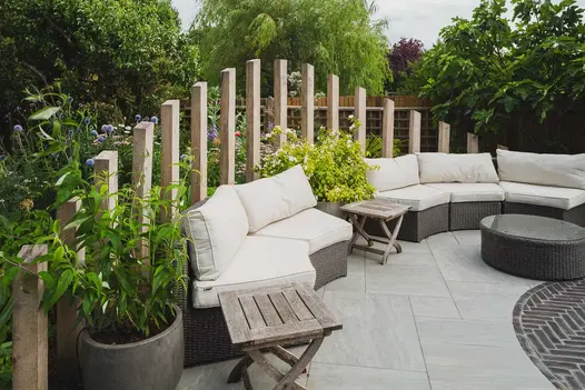Numerous wooden planks form beautiful feature behind seating area, with Kandla Grey Porcelain Paving used with grey clay paver circle.