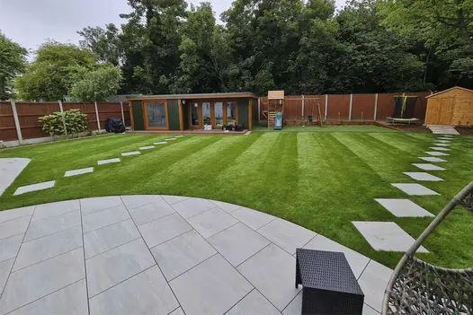 2 paths of Kandla Grey porcelain tiles set corner to corner, laid across lawn from curved-edged patio to garden buildings.